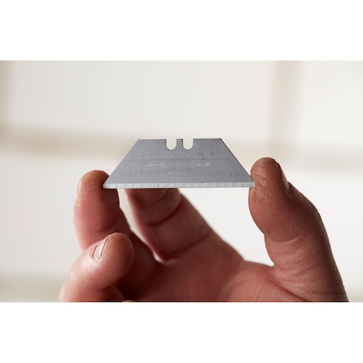 Photo of STANLEY 0-11-921 utility blade held between fingers, close-up of silver straight edge.