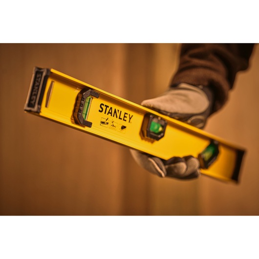 STANLEY 0-42-073 spirit level held in gloved hand, yellow body with visible bubble vial.