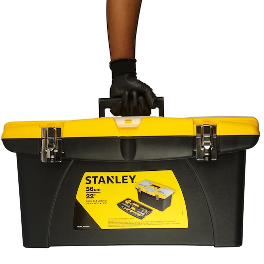 Stanley 1-92-908 tool box, yellow and black, front angle, held by gloved hand, white background.