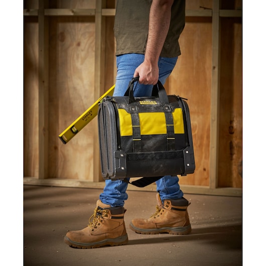 STANLEY 1-94-231 tool bag with yellow and black colors, carried by person on worksite, side view.