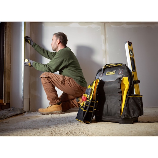 STANLEY 1-95-611 tool backpack with tools and level, shown upright on floor at construction site.