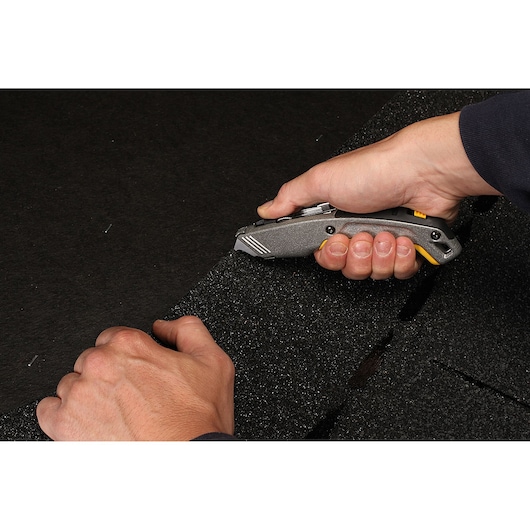 STANLEY 10-789 utility knife cutting thick black foam, handheld, close-up view.