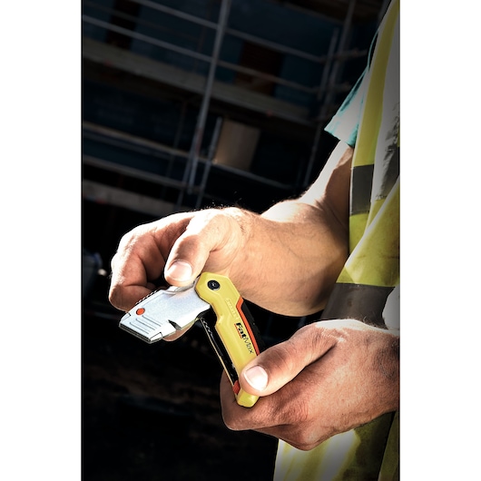 STANLEY 10-825 folding utility knife held in hand, yellow and silver design, construction site background.
