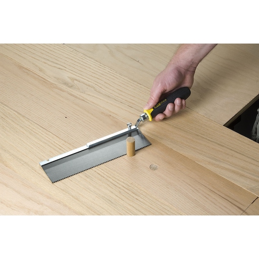 STANLEY 15-252K photography of flush cut saw with black handle cutting wooden dowel on light wood surface.