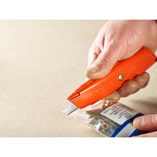 STANLEY 2-11-987 utility knife cutting plastic screw packaging, close-up showing orange handle and blade.