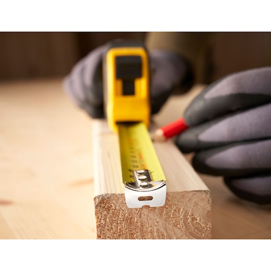 STANLEY 30-394 tape measure used to mark wood, close-up, with gloved hands and pencil.