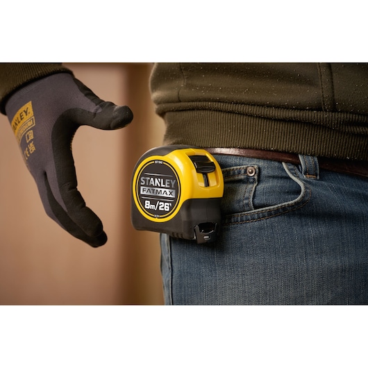 STANLEY 33-731 tape measure clipped to jeans pocket, hand wearing work glove nearby.