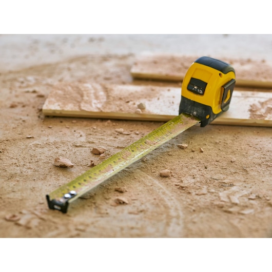 STANLEY 33-732 tape measure, yellow and black, extended on dusty construction floor with wood pieces.