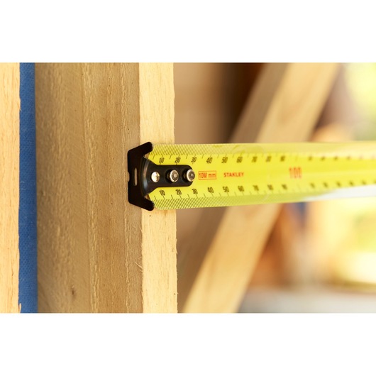 STANLEY 33-829 yellow tape measure in use measuring wooden beam, close-up photography.