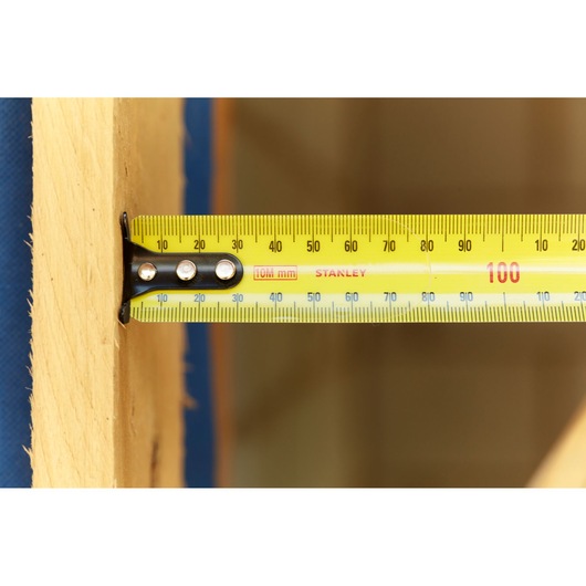 STANLEY 33-829 yellow tape measure in use measuring wooden plank, close-up side angle.