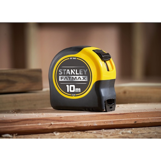 STANLEY 33-829 FATMAX 10m tape measure, black and yellow casing, photography on wood surface.