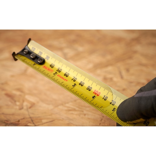 STANLEY 33-832 tape measure close-up, yellow blade with black markings, held by gloved hand.
