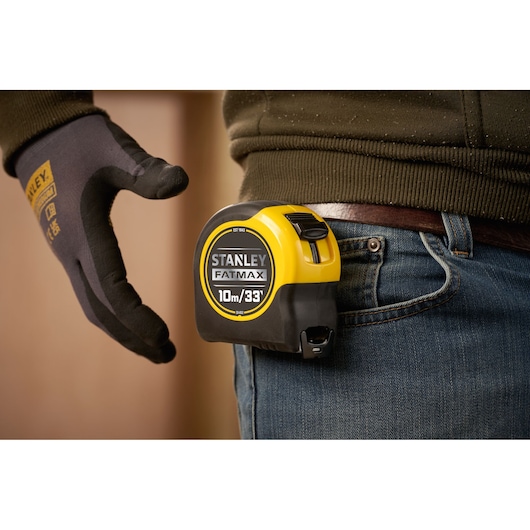 STANLEY 33-832 tape measure clipped on jeans belt, close-up side angle, yellow and black design.