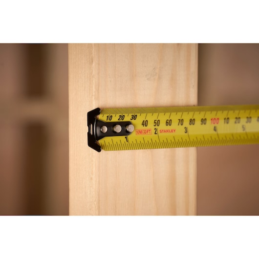 STANLEY 33-832 tape measure in use against wood, close-up photo showing yellow metric markings.