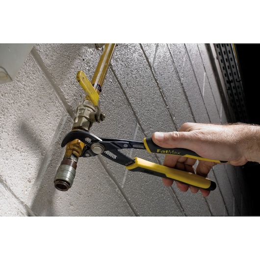 STANLEY 84-648 pliers with yellow and black handles gripping a metal pipe fitting near a wall.