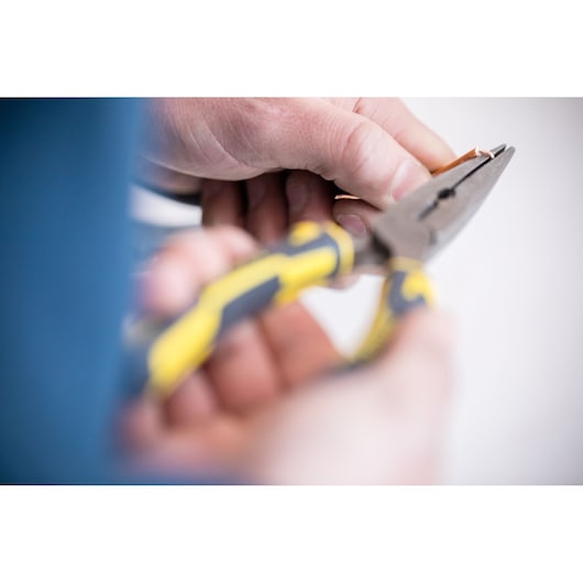 STANLEY 89-870 pliers with yellow and black handle held cutting copper wire, close-up photography.