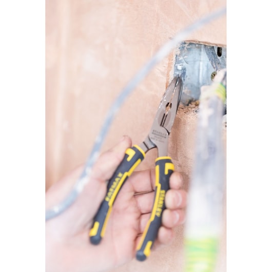 STANLEY 89-872 long nose pliers with black and yellow handles used for electrical work near a wall outlet.