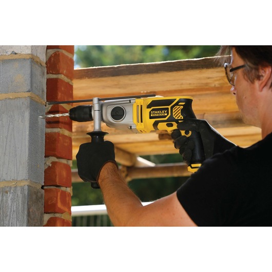 STANLEY FME142K hammer drill in use drilling into a brick wall, worker wearing gloves outdoors.