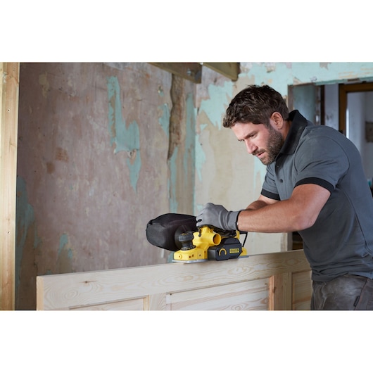Photo of STANLEY FME630 belt sander in use on wood surface during renovation, side view.