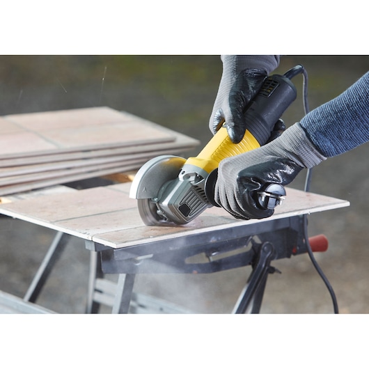 STANLEY FMEG220 angle grinder cutting tile, close-up, black and yellow tool held by gloved hands.