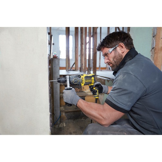 STANLEY FMEH850K hammer drill in use, drilling into a wall, construction site setting.