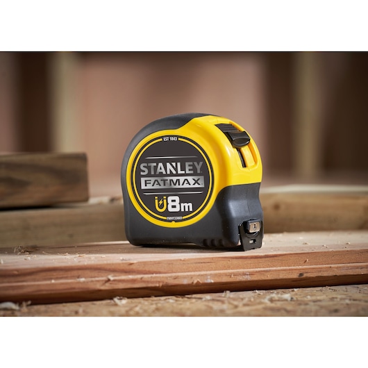 Stanley FMHT33869 FatMax magnetic tape measure 8m, yellow and black, side angle, on wood surface.