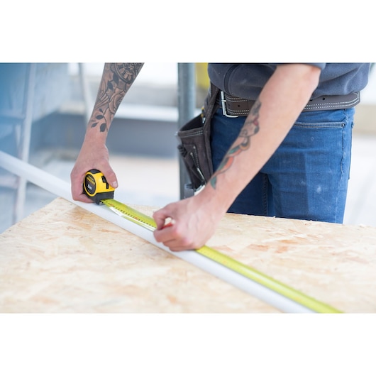 Photo of STANLEY FMHT36148-3 tape measure being used to measure a white strip on a wooden workbench.