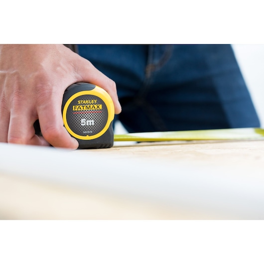Photo of STANLEY FMHT36148-3 FATMAX 5m tape measure held by hand on wood surface.