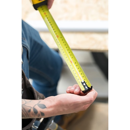 STANLEY FMHT36148-3 tape measure in use, extended by hand, yellow blade with clear markings.