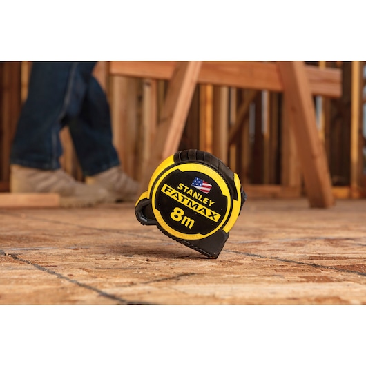 STANLEY FMHT36328 FATMAX 8m tape measure in yellow and black on a wooden floor at a construction site.