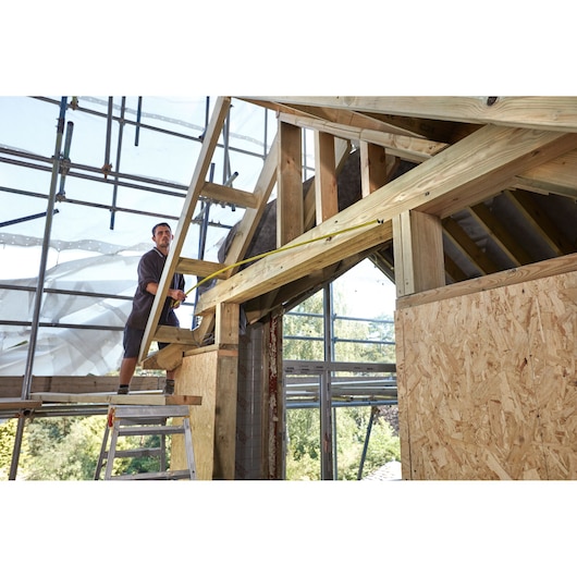 STANLEY FMHT36328 tape measure used by a worker measuring timber beams at a construction site.