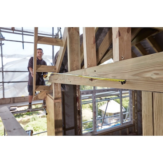 STANLEY FMHT36328 tape measure stretched along wooden beam at construction site, photo from side angle.