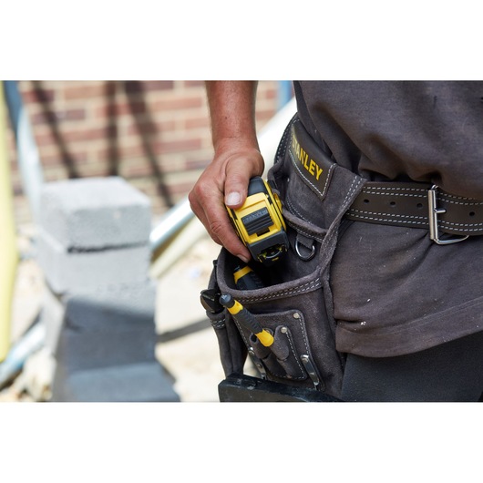 Photo of STANLEY FMHT36328 tape measure in a tool belt pouch at a construction site.