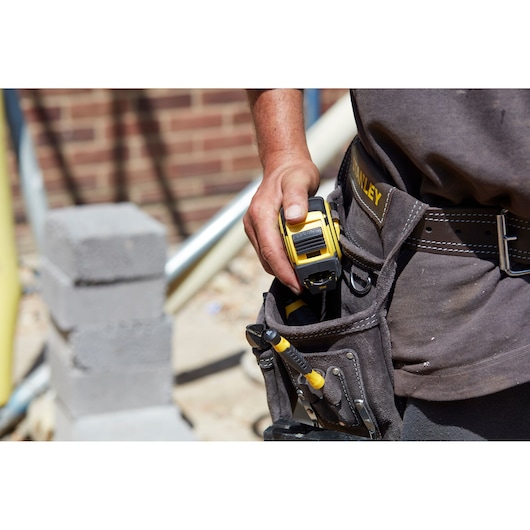 Photo of STANLEY FMHT36328 tape measure being placed in a tool belt at a construction site.
