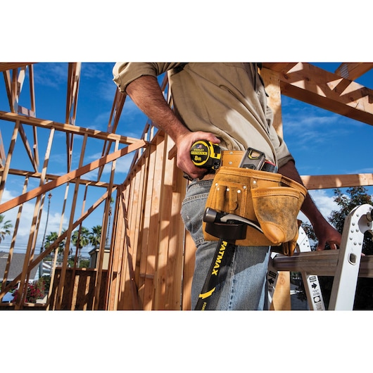 STANLEY FMHT36328 tape measure in yellow and black held by worker on construction site, tool pouch visible.