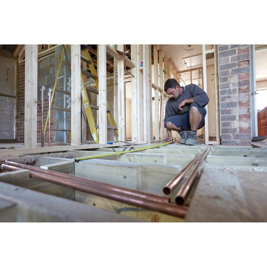STANLEY FMHT36328 tape measure used by worker in home construction, tape extended across wooden floor framing.