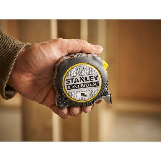 Stanley FMHT38219-3 FATMAX tape measure, 8m length, gray and yellow, held in hand, product photography.