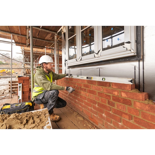 STANLEY FMHT43679-1 spirit level used by a builder on a brick wall at a construction site, side angle.