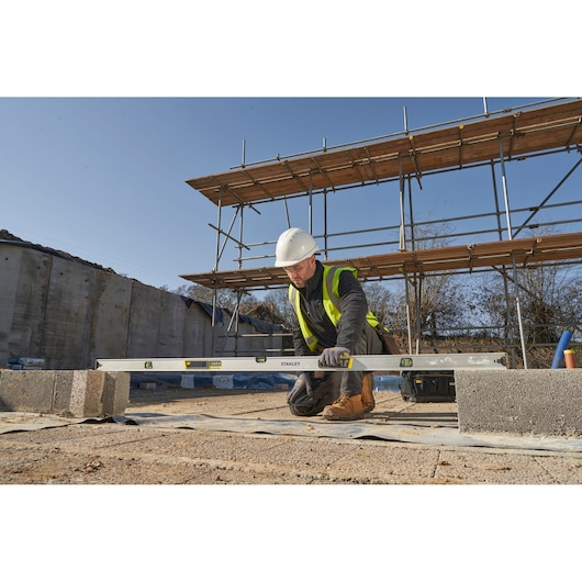STANLEY FMHT43679-1 spirit level used by builder on construction site with blocks and scaffolding in background.