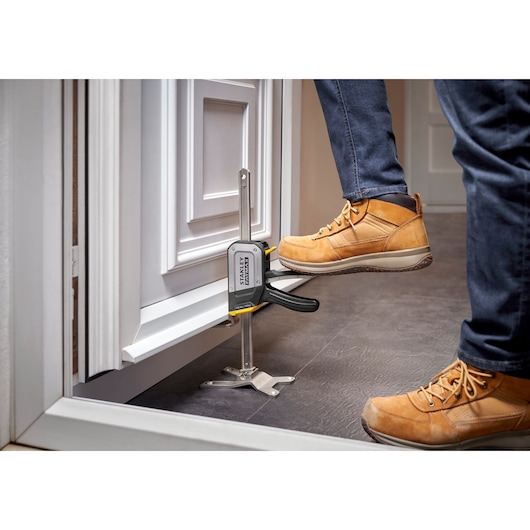 STANLEY FMHT83550-1 door installation tool clamping cabinet, worker using foot pedal, product photography.