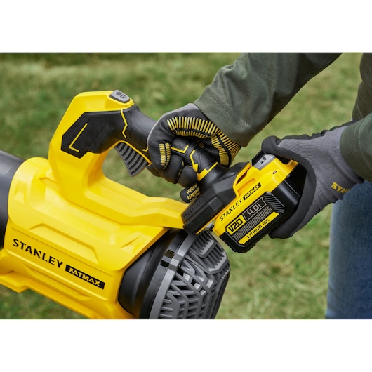 STANLEY SFMCBL730B leaf blower close-up, yellow handle and battery, outdoor use, person with gloves.