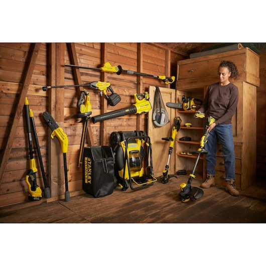 Photo of STANLEY SFMCBL7B garden power tools set displayed in wooden shed, various yellow tools and storage bag.