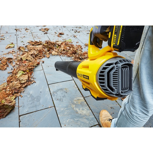 STANLEY SFMCBL7M1 cordless leaf blower close-up, yellow and black, blowing leaves on stone tiles.