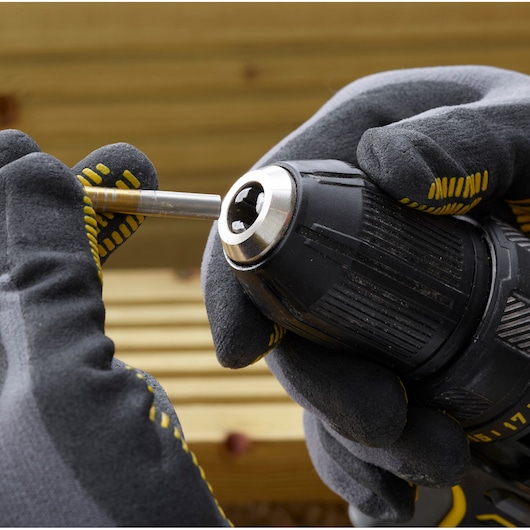STANLEY SFMCD700D2S drill photographed close-up, gloved hands inserting a drill bit outdoors.