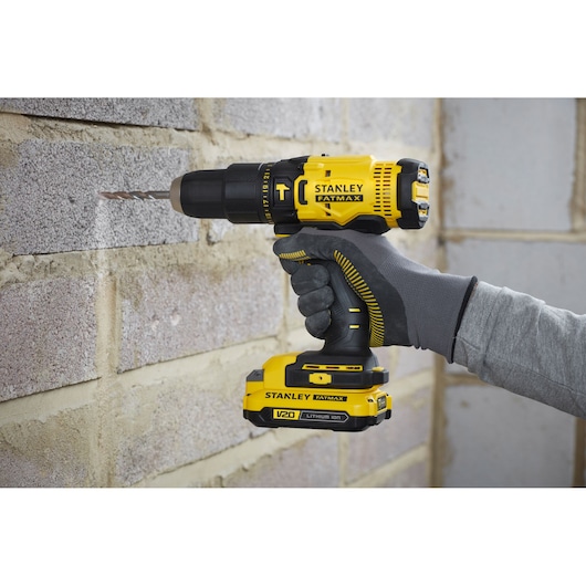 Stanley SFMCD711DM2 drill in use, yellow and black, drilling into brick wall, photography side angle