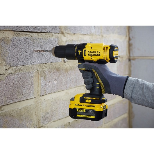 Stanley SFMCD711M1 cordless drill in use on a brick wall, side view, yellow and black, V20 4.0Ah battery.