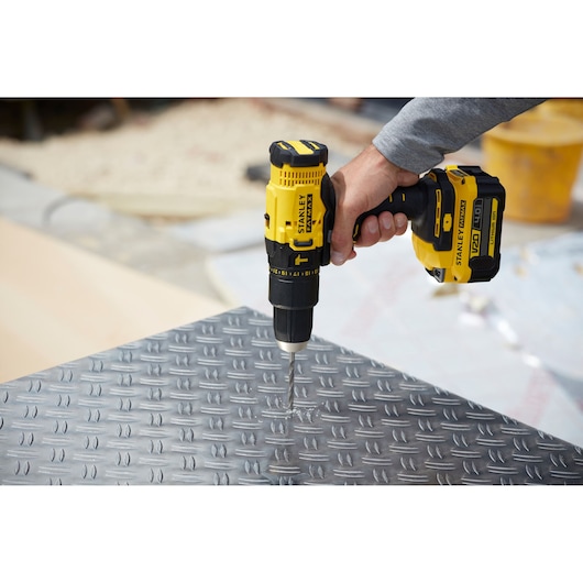 STANLEY SFMCD711M1 cordless drill being used to drill into metal plate, close-up side angle.