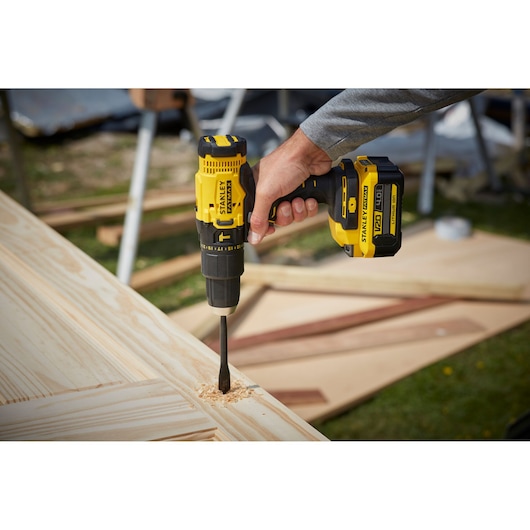 STANLEY SFMCD711M1 cordless drill in use, drilling into light wood panel outdoors.
