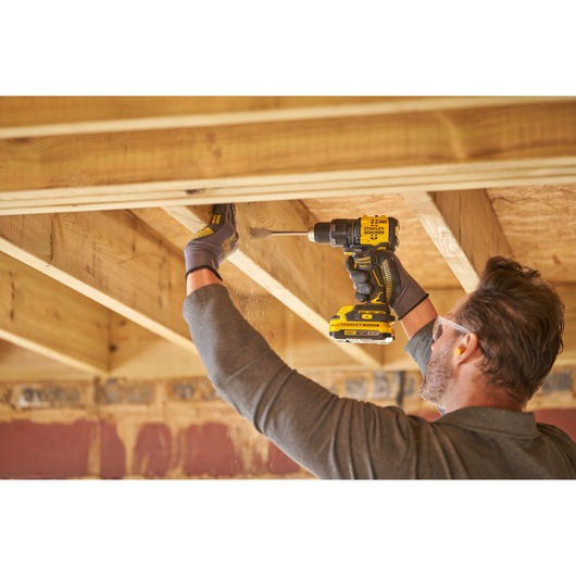 STANLEY SFMCD716B-XJ cordless drill in use by a person drilling wood beams indoors, side view.