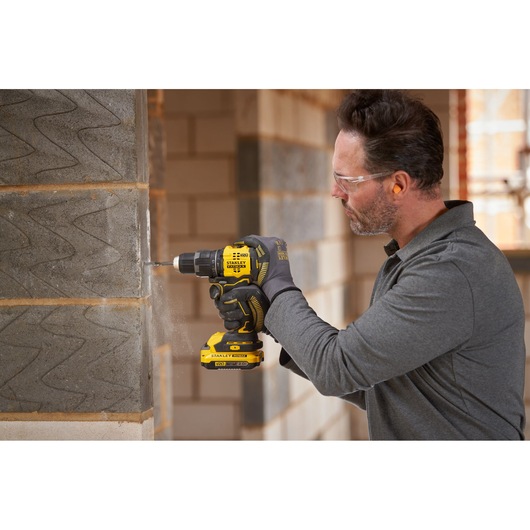 Photo of STANLEY SFMCD716B-XJ cordless drill being used to drill into a concrete wall on a construction site.